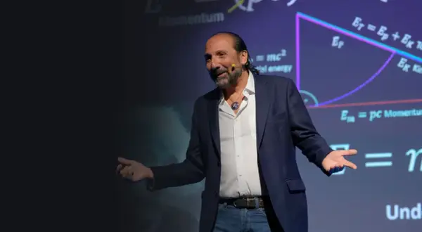 Nassim Haramein, con gestos amplios, explica conceptos de física ante una pantalla con fórmulas como E=mc².