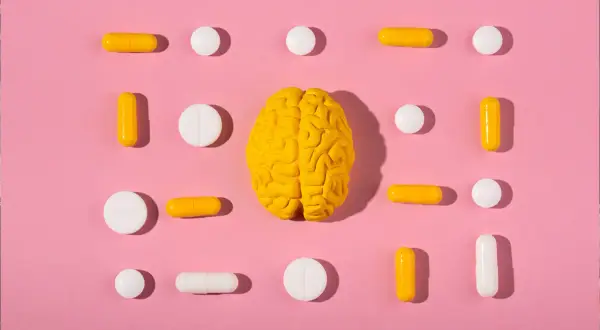 Żółty model mózgu otoczony białymi i żółtymi tabletkami i kapsułkami. Czy to symbol wsparcia dla serotoniny?