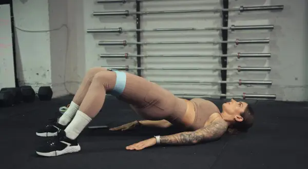 Kobieta wykonuje ćwiczenie glute bridge z taśmą oporową na udach.