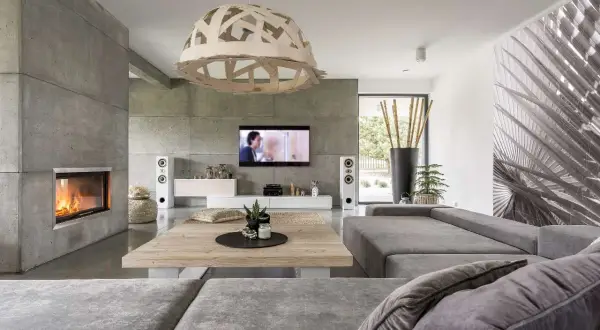 Nowoczesny salon z kominkiem i ścianą z betonu architektonicznego. Szara kanapa, drewniany stolik i designerska lampa tworzą przytulną atmosferę.