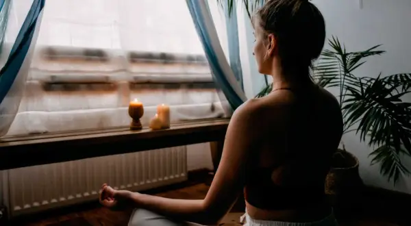 Mujer meditando en un espacio para meditar en casa, con velas encendidas y plantas.
