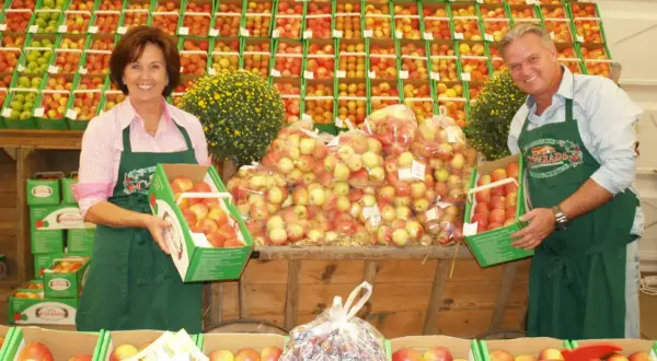 Ein Paar präsentiert Äpfel auf dem markt leichlingen. Sie halten Kisten mit frischen Äpfeln, umgeben von weiteren Obstkisten.