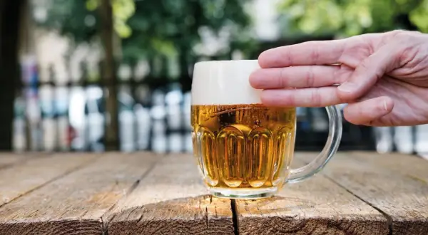 Dłoń dotyka gęstej piany na kuflu piwa, pokazując, jak powstaje piana.