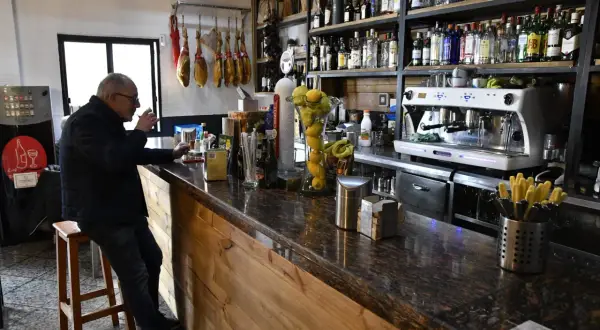 Hombre en taburete en bar Almería Enix, con jamones colgados y estanterías llenas de licores.