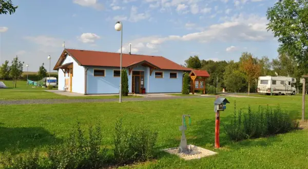 Ein hellblaues Gebäude mit rotem Dach auf dem Camping Vaclav. Wohnmobile und Zelte sind auf dem Rasen zu sehen.