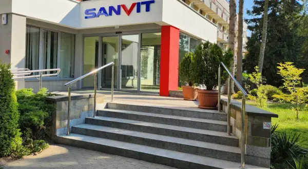 Wejście do sanatorium Sanvit w Ciechocinku. Schody prowadzą do przeszklonych drzwi, a nad nimi widnieje niebiesko-czerwone logo.