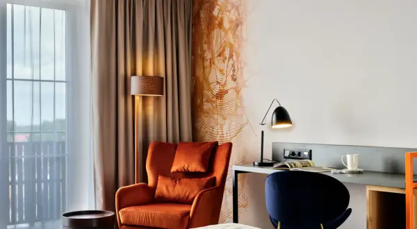 Przytulny pokój w **Bergo Hotel Szklarska Poręba**: pomarańczowy fotel, biurko z lampką i granatowe krzesło.