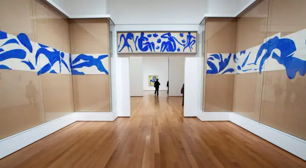 Gallery hallway showcasing Henri Matisse obras: blue cut-outs of figures adorn the walls, with a long horizontal piece above an archway and flowing designs on either side.