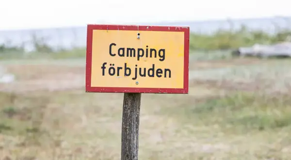 Gul skylt med texten "Camping förbjuden" på en trästolpe. Ingen husbil parkering här.