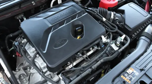 Silnik EcoBoost w Fordzie Escape 2020. Widoczna pokrywa silnika z logo Ford i napisem EcoBoost, akumulator i elementy układu dolotowego.