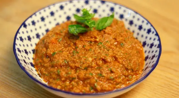 Un cuenco de pesto rosso casero, con hojas de albahaca fresca encima, listo para acompañar pasta o bruschetta.