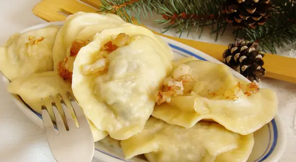 Pyszne pierogi z mięsem i kapustą, okraszone skwarkami, na talerzu z gałązką sosny i szyszkami.