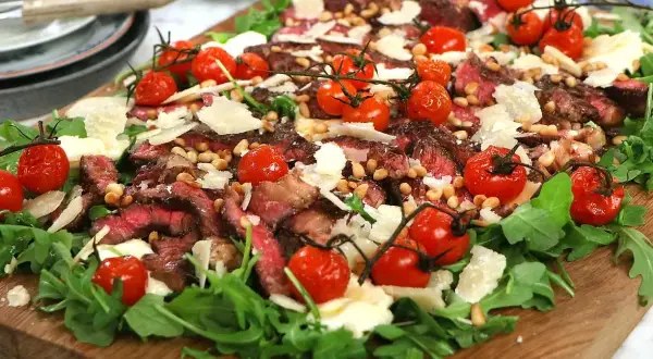 En läcker tagliata med mört oxkött, körsbärstomater, pinjenötter och parmesan på en bädd av ruccola. Ett perfekt tagliata recept!