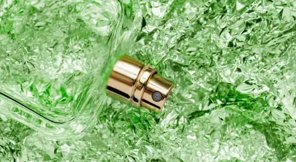 Złota pompka perfum na tle pogniecionej, zielonej folii. Zapach wetywerii unosi się w powietrzu.