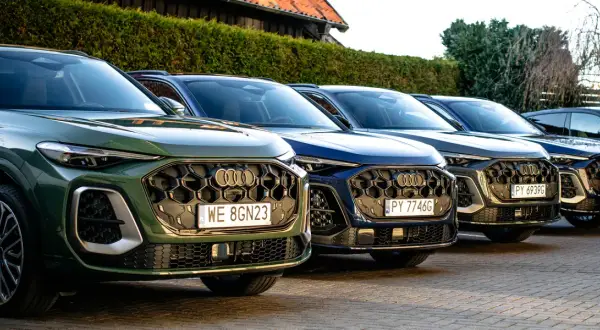 Rząd nowych Audi Q5 w różnych kolorach, od zielonego po ciemne odcienie, zaparkowanych na zewnątrz.