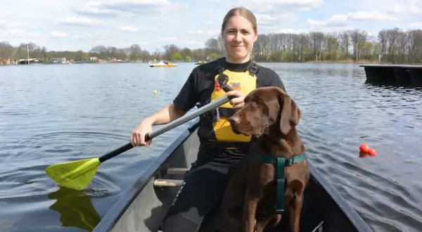 Frau und brauner Hund genießen das Kanufahren mit Hund auf einem sonnigen See.