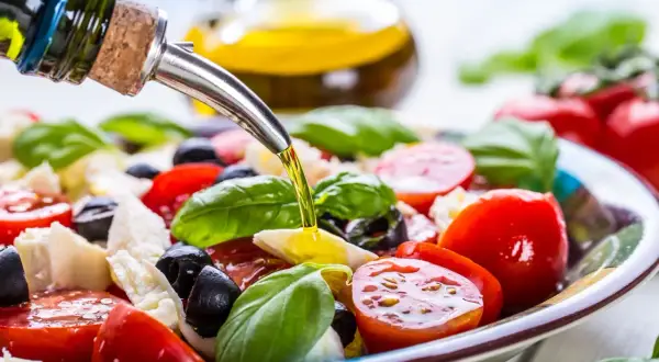 Sałatka caprese z pomidorów, mozzarelli, oliwek i bazylii, polana oliwą z oliwek. Idealna na zdrową dieta śródziemnomorska.
