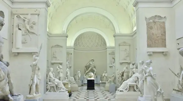 Interno della Galleria dell'Accademia con sculture classiche in marmo bianco, pavimentazione a scacchi e soffitto a volta.