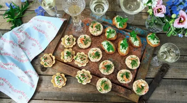 Små, läckra tilltugg till bubbel, serverade på en rustik bricka med blommor och glas. Perfekt för festliga stunder.