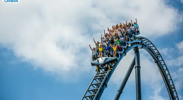 Ludzie krzyczą z radości na pokładzie Hyperiona, największego rollercoastera w Polsce, pędząc po stalowych torach na tle błękitnego nieba.