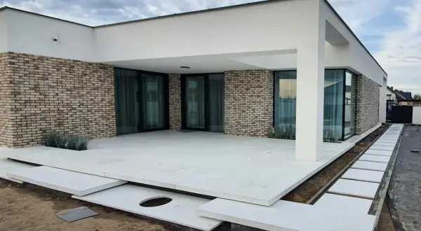Nowoczesny dom z ceglaną elewacją i tarasem z jasnego, **betonu szczotkowanego**.