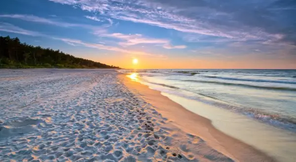 Zachód słońca nad morzem, piaszczysta plaża z śladami stóp, las w tle. Idealne, fajne miejsce nad morzem dla dwojga na romantyczny spacer.