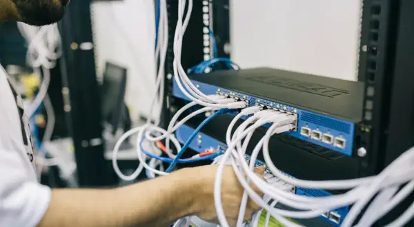 Technik podłącza kable do switcha sieciowego. Każde urządzenie ma swój unikalny adres MAC, który identyfikuje je w sieci.