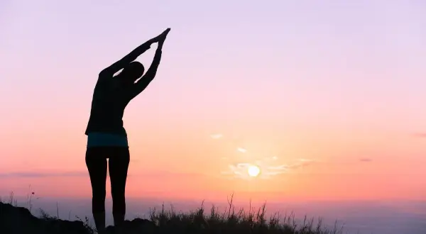 Silueta de una persona en postura de yoga al amanecer, sintiendo la energía vital del nuevo día.
