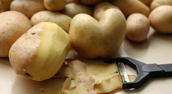 Obieraczka do ziemniaczków leży obok świeżo obranych ziemniaków. Skórki tworzą na blacie małą górkę.