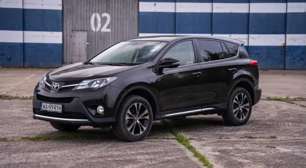 Czarny, używany Toyota RAV4 z salonu, zaparkowany przed budynkiem z numerem 02.