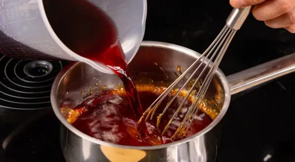 Flüssigkeit wird in einen Topf mit karamellisiertem Zucker gegossen, während ein Schneebesen umrührt, um eine Balsamico-Creme herzustellen.