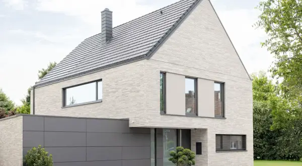 Modernes Haus mit hellem Klinker, das nicht gestrichen ist. Graues Dach, Garage und Fensterrahmen.