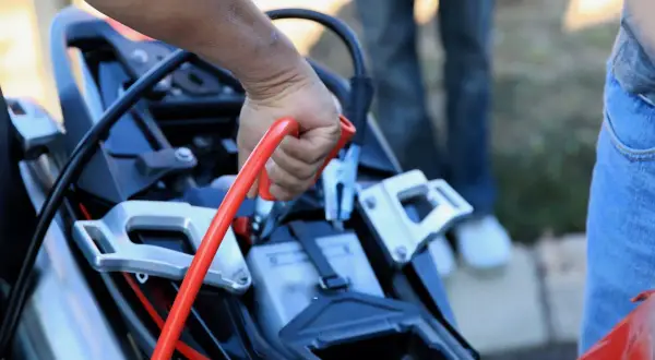 Mano sujetando pinza roja para desconectar batería moto.