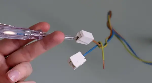 Hand prüft Kabel mit Schraubendreher, um eine Lampe anzuklemmen.