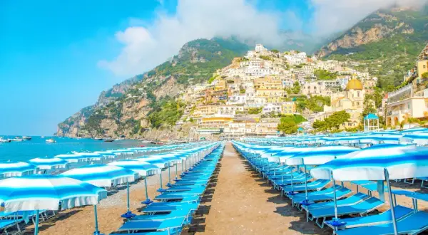 Rzędy leżaków i parasoli na plaży w Positano. W tle malownicze, kolorowe domy wznoszące się na zboczu góry. Idealne miejsce, by zobaczyć piękno Amalfi.