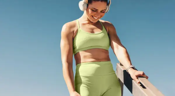 Lächelnde Frau mit Kopfhörern, die eine Pause beim Krafttraining genießt. Ein Tag Pause reicht, um neue Energie zu tanken.