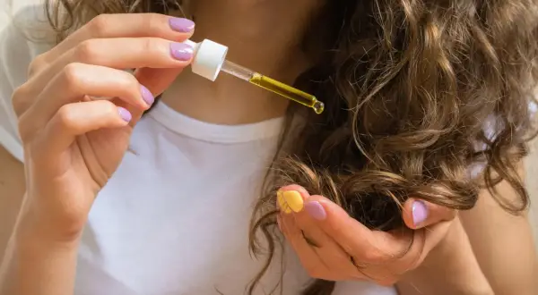 Frauenhand mit Pipette, die Rizinusöl auf ihr lockiges Haar tropft. Die natürliche Castor oil wirkung für Glanz und Pflege.