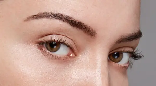 Gros plan sur des yeux marron avec des cils longs. Le sourcil gauche est légèrement plus fin, montrant comment dessiner ses sourcils pour un look naturel.