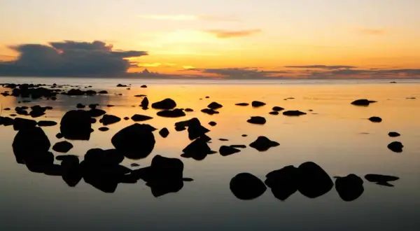 Solnedgång över havet med stenar i förgrunden. Perfekt för gotland tips.