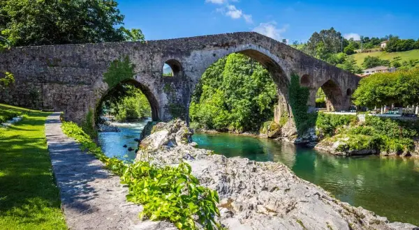 El histórico puente de Cangas de Onís cruza un río de aguas cristalinas rodeado de exuberante vegetación.