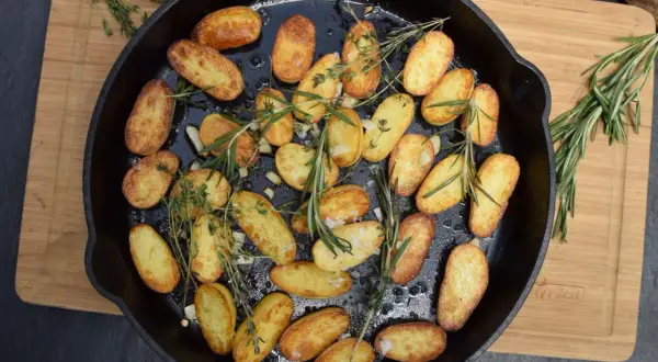 Goldbraune rosmarin kartoffeln mit Knoblauch und Kräutern in einer Gusseisenpfanne, bereit zum Servieren.