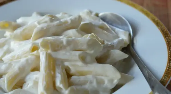 Penne z kremowym twarogiem na słodko, podane na talerzu z łyżką. Pyszne danie, które z pewnością zadowoli każdego.
