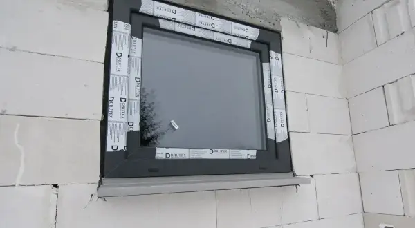 Nowe okno w szarej ramie, otoczone taśmą montażową. Rozważasz wymiana okien cena? To dobry moment na inwestycję.