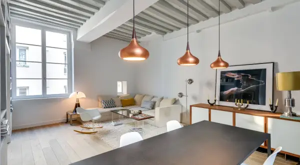 Lámparas colgantes de cobre y un diseño moderno reflejan las **últimas tendencias iluminación salones**. Un sofá blanco y una mesa de comedor completan el espacio.