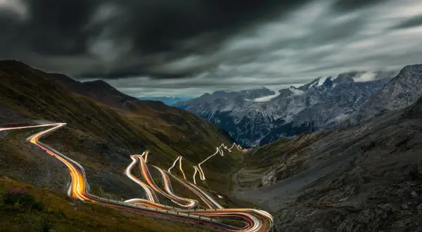 Ślady świateł samochodów wiją się serpentynami na stromych zboczach górskich, tworząc świetlisty szlak na przełęczy Stelvio.
