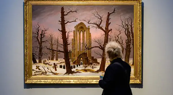 Besucherin betrachtet Caspar David Friedrichs "Abtei im Eichwald" in der Alten Nationalgalerie. Ein winterliches Motiv mit Ruinen und Kreuzen.