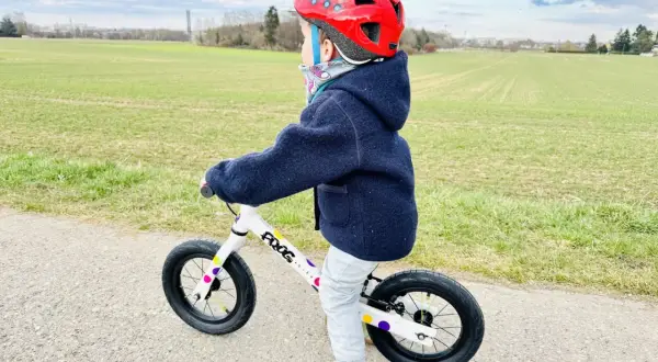 Kind mit rotem Helm übt das laufrad fahren auf einem Feldweg.
