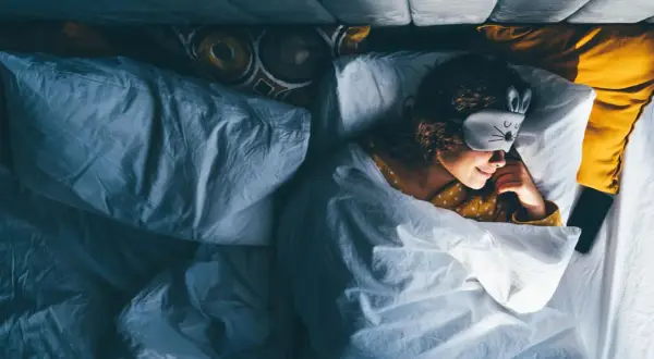 Ein Mädchen mit Hasen-Schlafmaske liegt im Bett und scheint schnell einschlafen zu wollen.