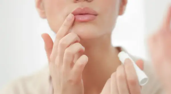 Mujer aplicándose bálsamo labial para el cuidado de labios.