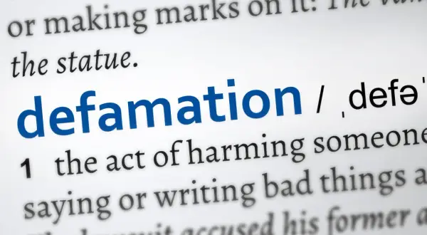 Słownikowa definicja "defamation" (zniesławienia), opisująca szkodzenie komuś przez mówienie lub pisanie złych rzeczy. Uważaj na pomówienia w pracy.